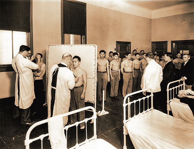 Enlargeable black and white photo of doctors examining a long line of immigrant men