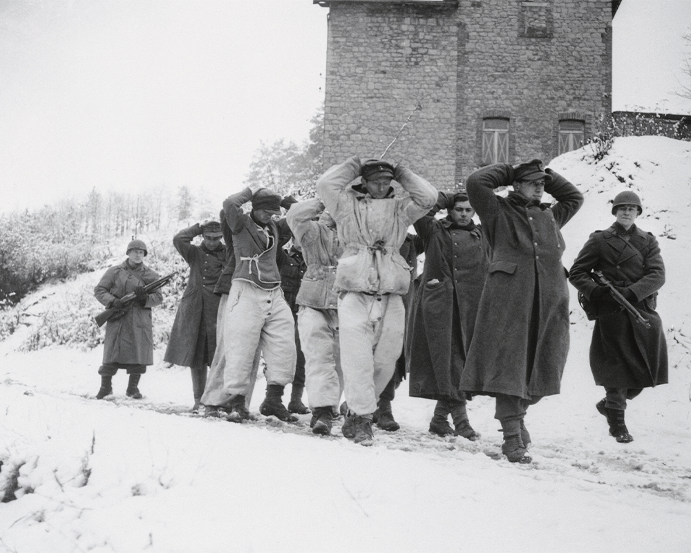 Black & white photo of soldiers in a snowy landscape walking with hostages