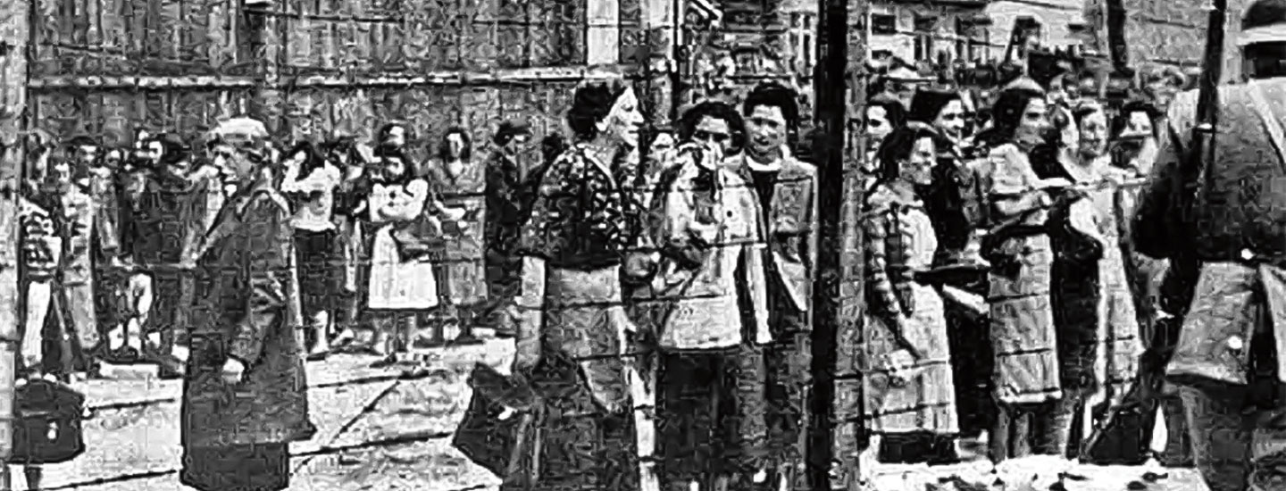 Black & white photo of Jewish families standing behind barbed-wire fence