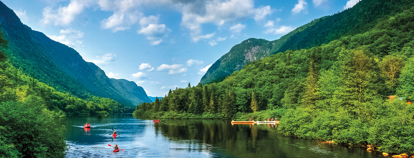People rowing kayaks, with woods and mountains all around them
