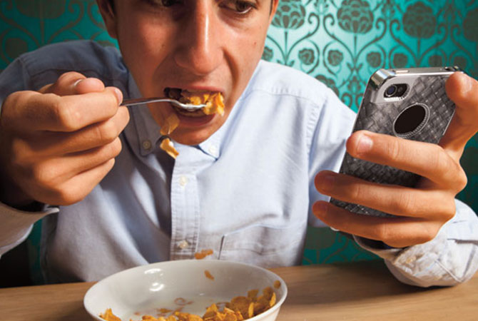 A teenage boy eating cereal while staring at his phone